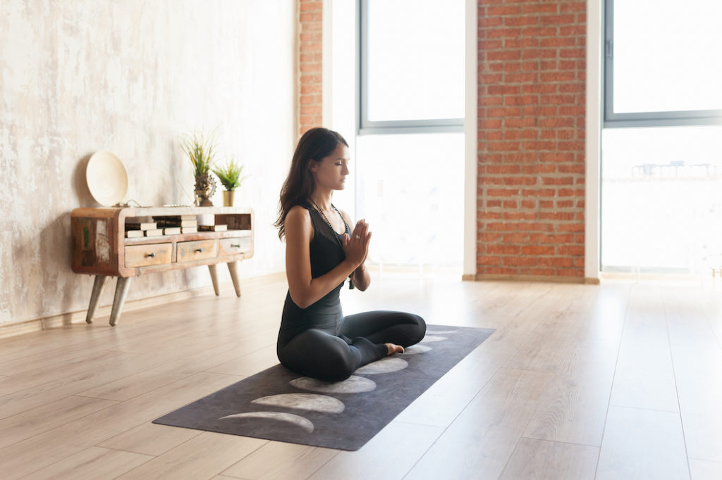 Bohemian woman doing yoga in minimalist boho apartment.