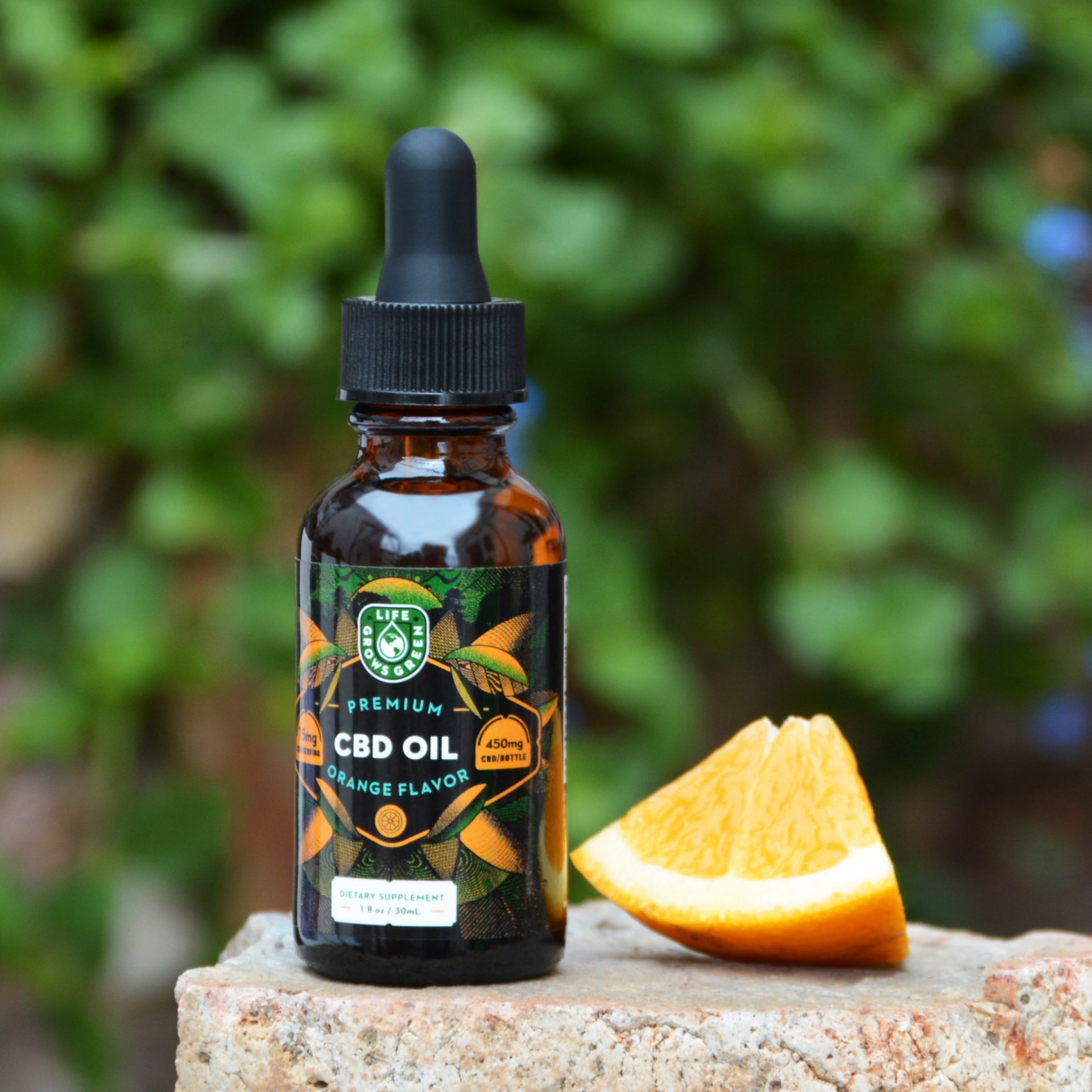 A bottle of Life Grows Green orange flavored CBD oil next to an orange slice.
