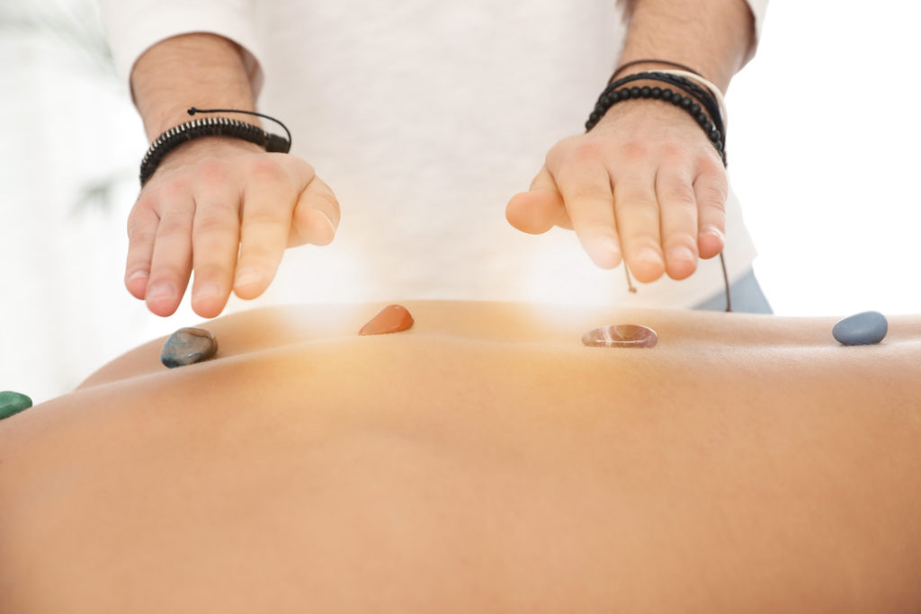 Hands above a person's back receiving Reiki with crystals. 