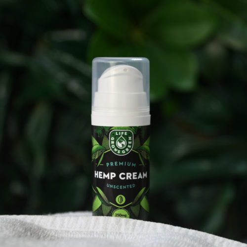 A bottle of hemp cream with a white towel in front of a green leafy background.