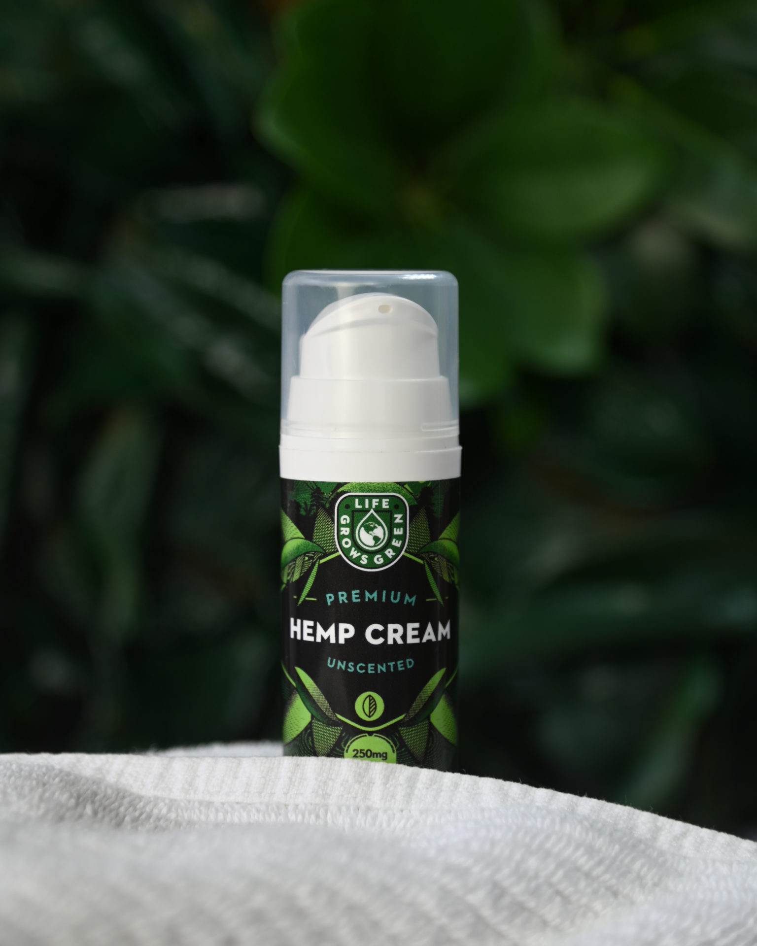 A bottle of hemp cream with a white towel in front of a green leafy background.