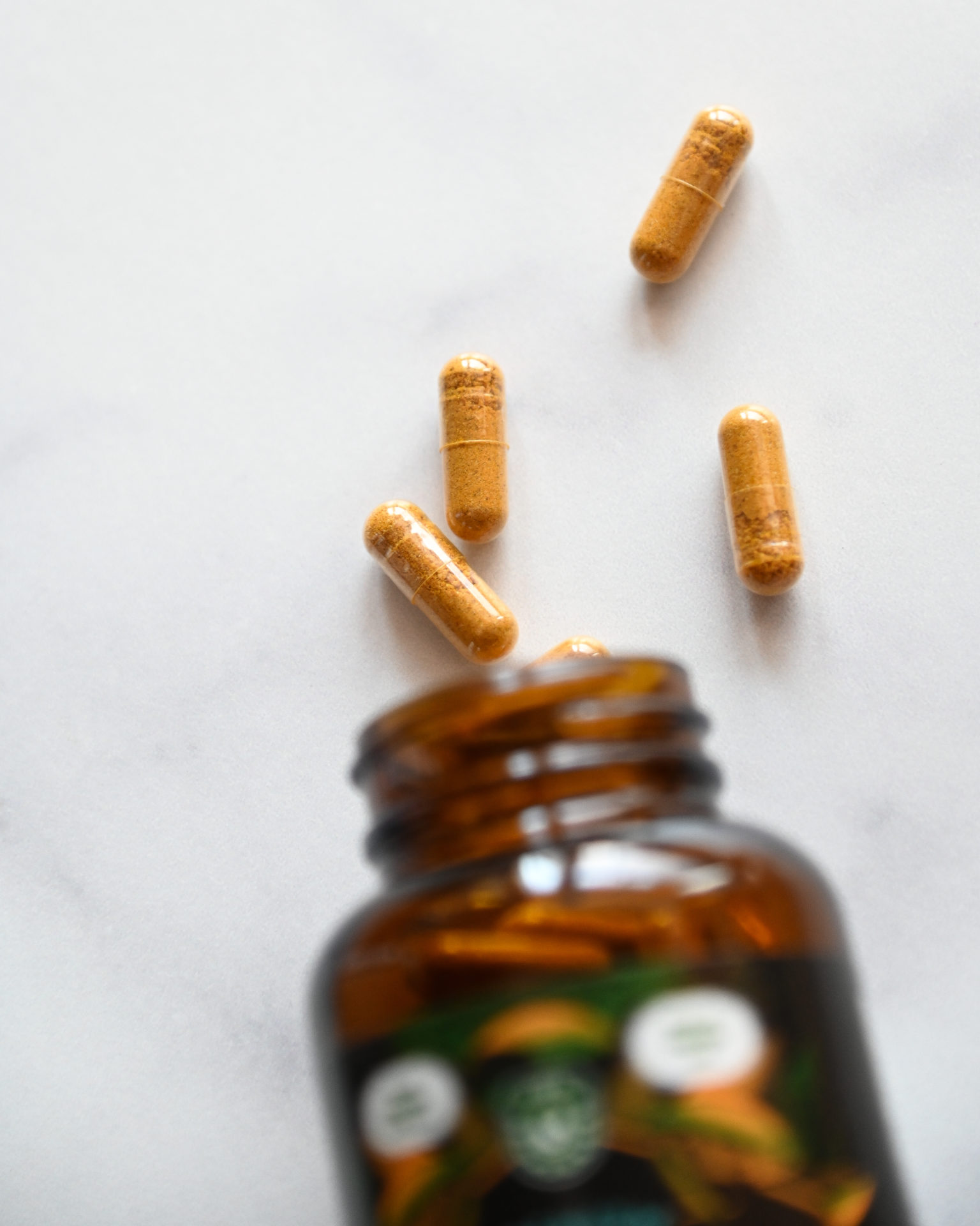 A bottle of hemp capsules with turmeric spilling out on a counter.