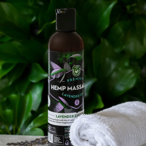 A bottle of hemp massage oil with lavender flowers and a spa towel.