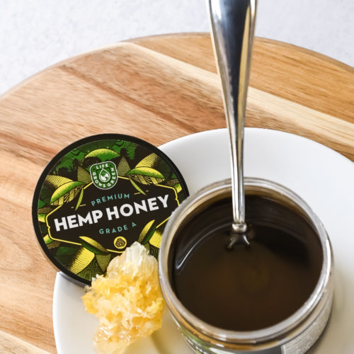 A jar of hemp honey with a spoon and a honeycomb.